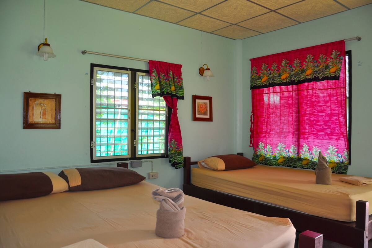 Une chambre avec deux lits, une fenêtre avec un rideau rouge et un luminaire fixé au mur.