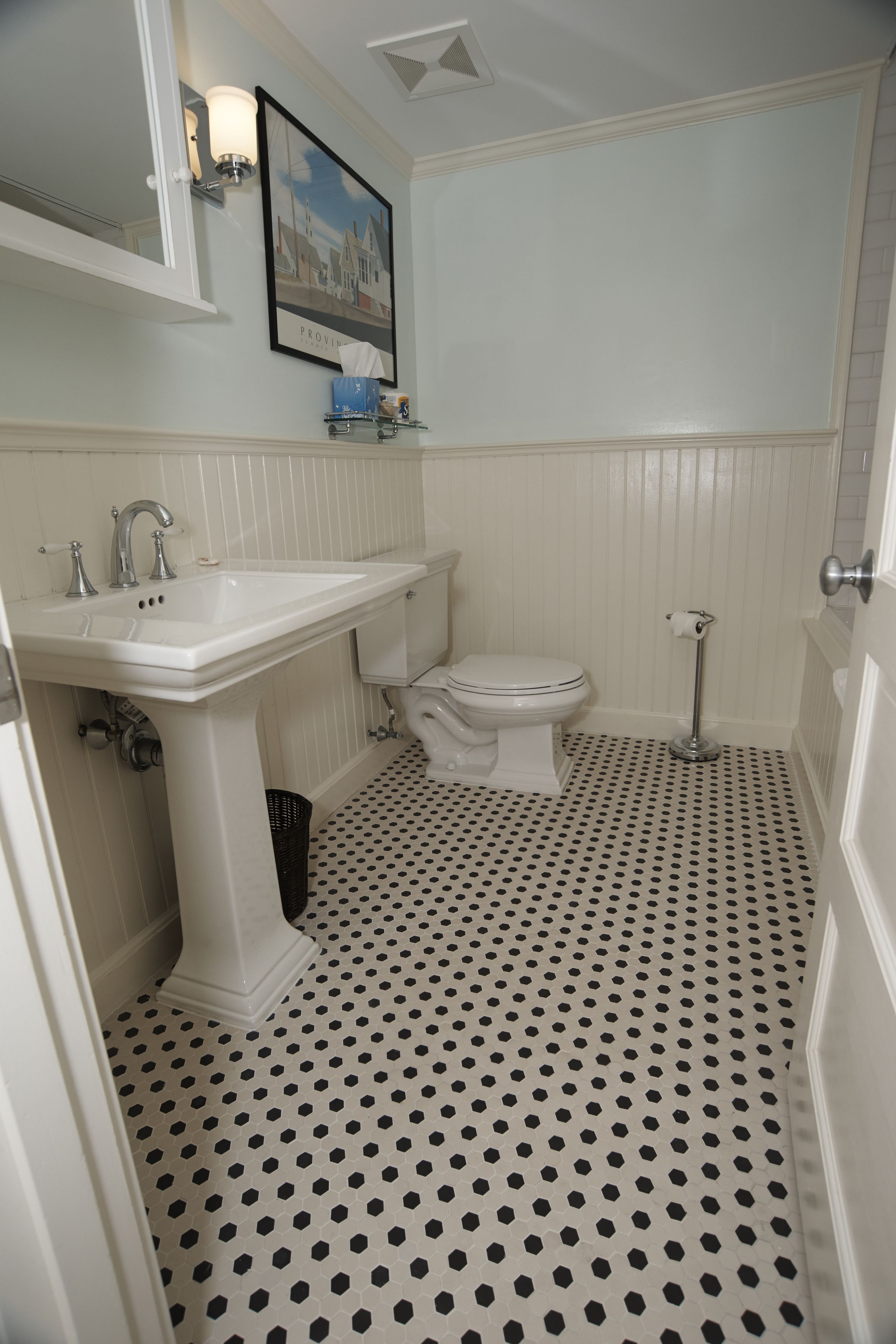 A bathroom with a white sink, toilet, and pedestal vanity. The floor has a black and white polka dot pattern.