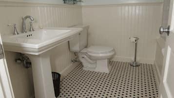 A bathroom with a white sink, toilet, and pedestal vanity. The floor has a black and white polka dot pattern.