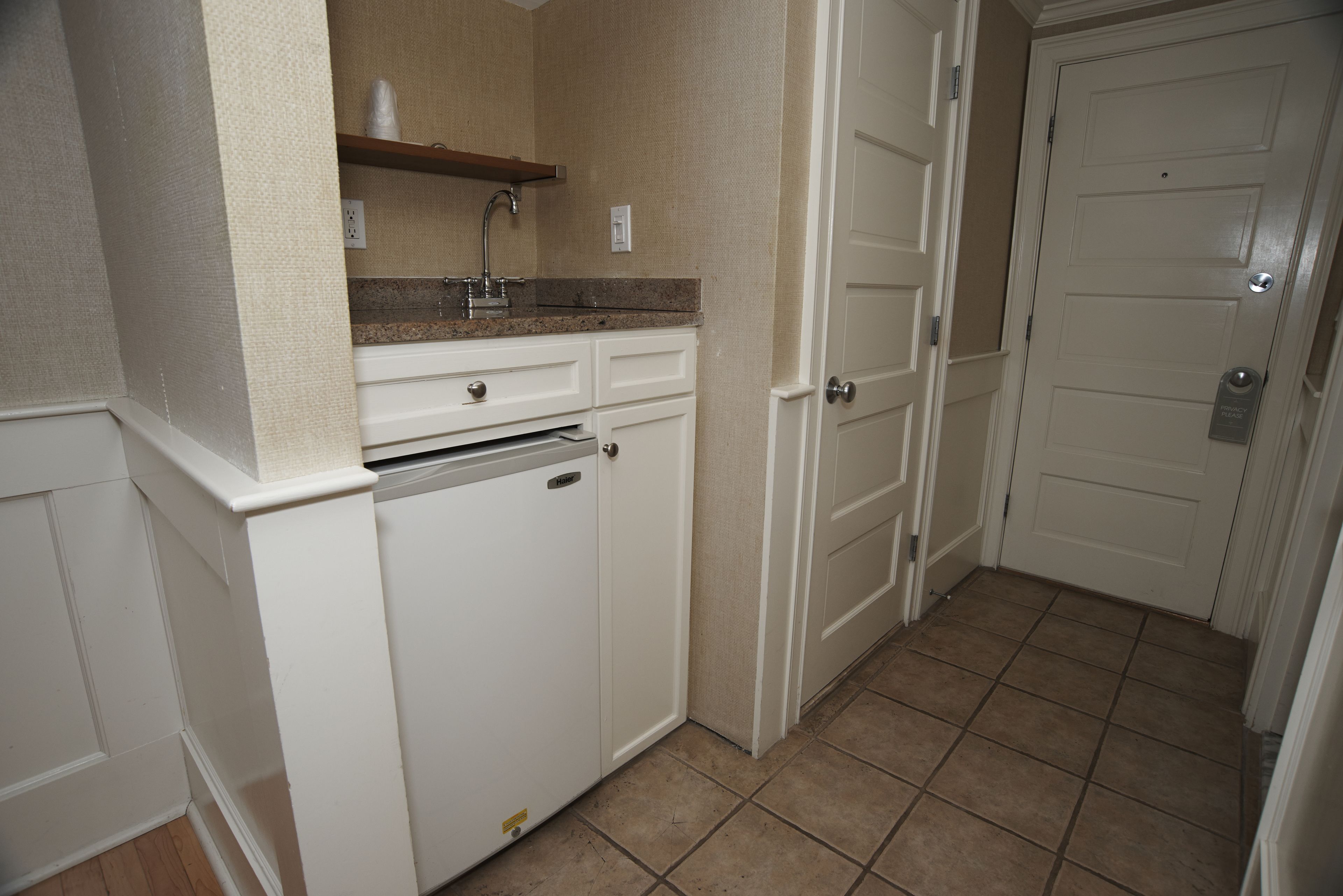 A compact kitchen with a built-in dishwasher, a countertop sink, and a small shelf above it.