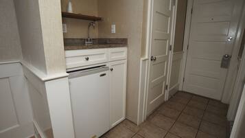A compact kitchen with a built-in dishwasher, a countertop sink, and a small shelf above it.