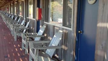 A row of white Adirondack chairs under a covered porch with a blue door marked with the number 124.