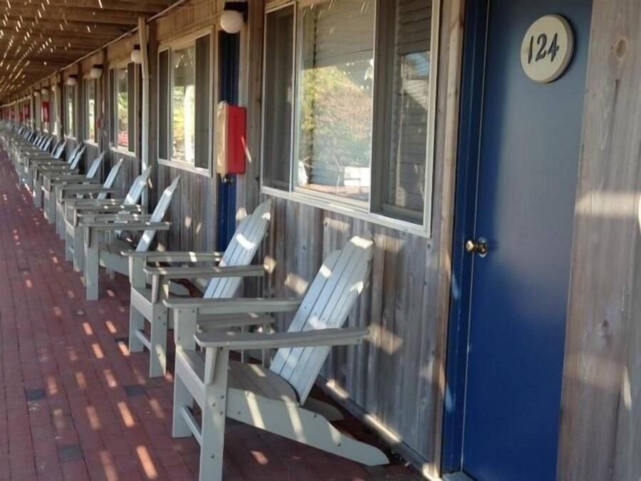 A row of white Adirondack chairs under a covered porch with a blue door marked with the number 124.
