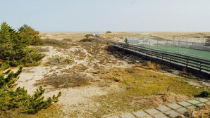 Ein Küstenpfad mit einer Holzbrücke, die zu einem grünen Sportplatz führt.
