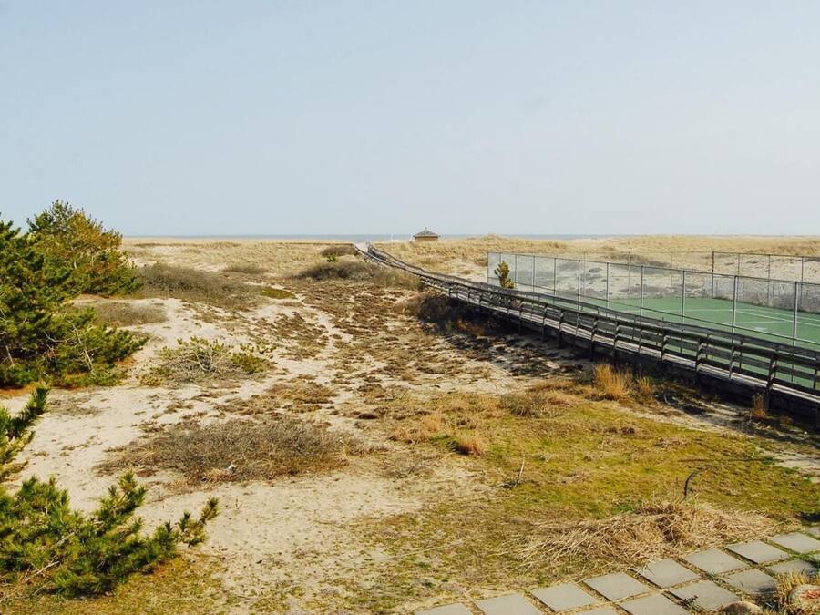Un sendero costero con un puente de madera que lleva a una cancha deportiva verde.