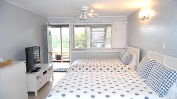 A bedroom with a bed, a television on a dresser, a ceiling fan, and a window with blinds.