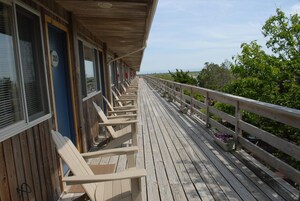 A wooden deck with rows of chairs, a railing, and a view of the sea.