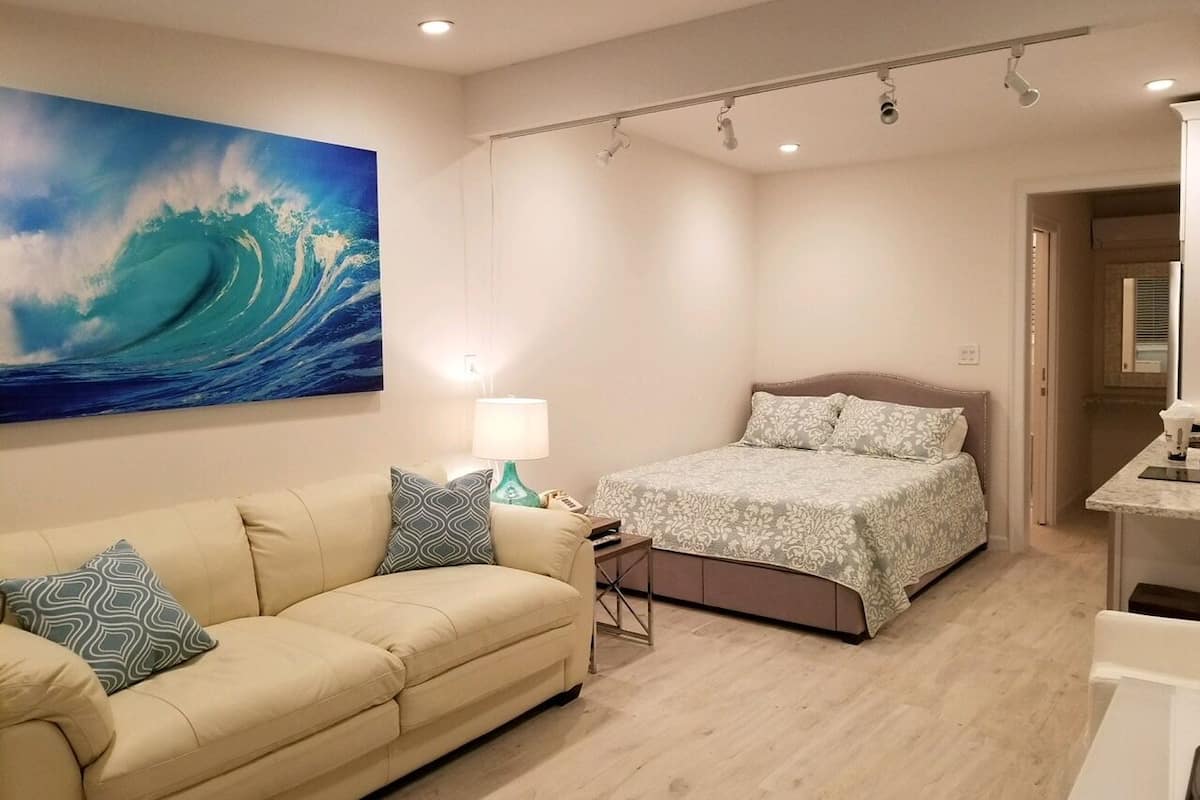 Een slaapkamer met een bed, een slaapbank, een nachtkastje en een schilderij van een golf aan de muur.