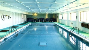 Ein großes Hallenbad mit mehreren Bahnen, Sicherheitshinweisen und einer mit sechseckigen Mustern gefliesten Wand.