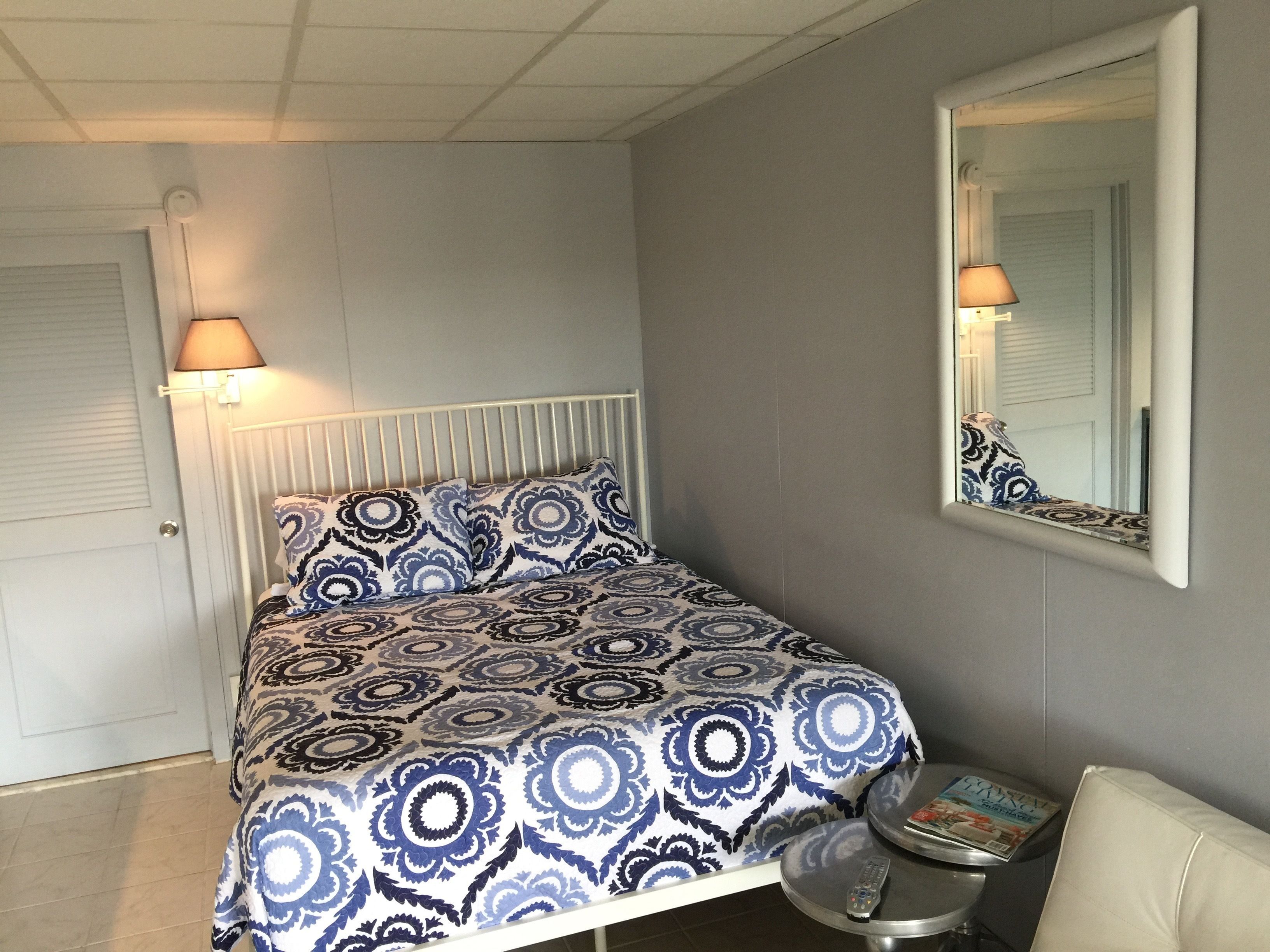 Et soveværelse med en seng, en sengetavlelampe og et lille bord med en fjernbetjening.