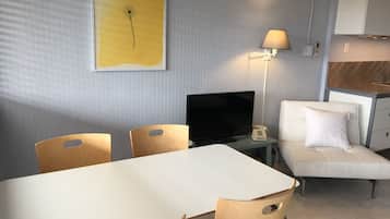 Habitación de hotel con una mesa de comedor, dos sillas, un televisor, una lámpara de noche, un sofá y un armario.