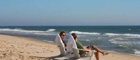 En strandscen med en person som sitter på en strandstol och en annan person som ligger på sanden.