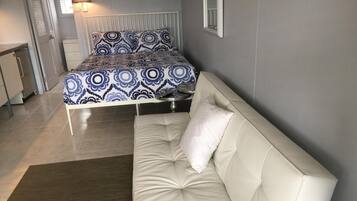 A bedroom with a bed, a white sofa, a rug, and a bedside table.