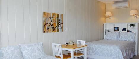 A room with two beds, a desk with chairs, a ceiling fan, wall-mounted lamps, and a wall art piece.
