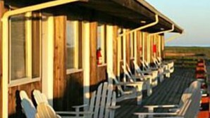 Eine Holzterrasse mit Adirondack-Stühlen und Tischen, mit Blick auf eine malerische Landschaft.