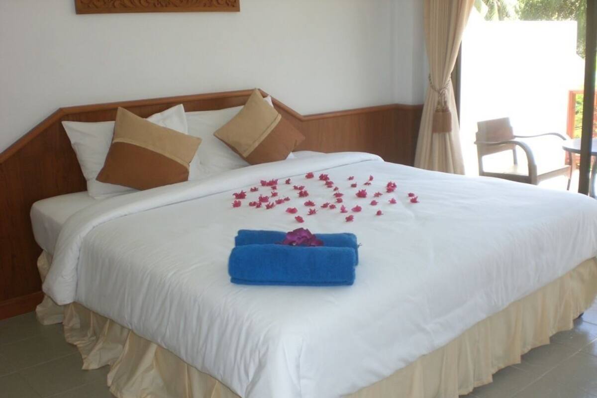 Un lit bien fait, avec des draps blancs, une serviette bleue et des pétales de fleurs roses.
