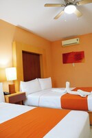 Quarto de hotel com duas camas, um ventilador de teto, um ar condicionado e uma mesa de cabeceira com luminária.