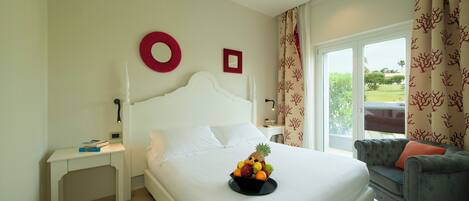 A hotel room with a bed, a bedside table, a fruit bowl, a grey sofa, and a view of the outdoors.