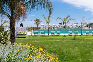 A poolside area with lounge chairs, a palm tree, and a clear blue sky.