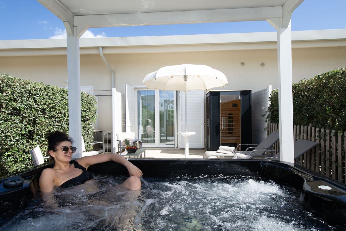 A person relaxing in a hot tub with a white umbrella and lounge chairs in the background.