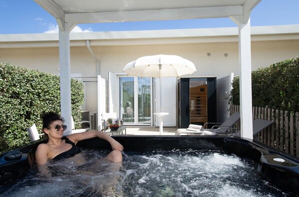 A person relaxing in a hot tub with a white umbrella and lounge chairs in the background.