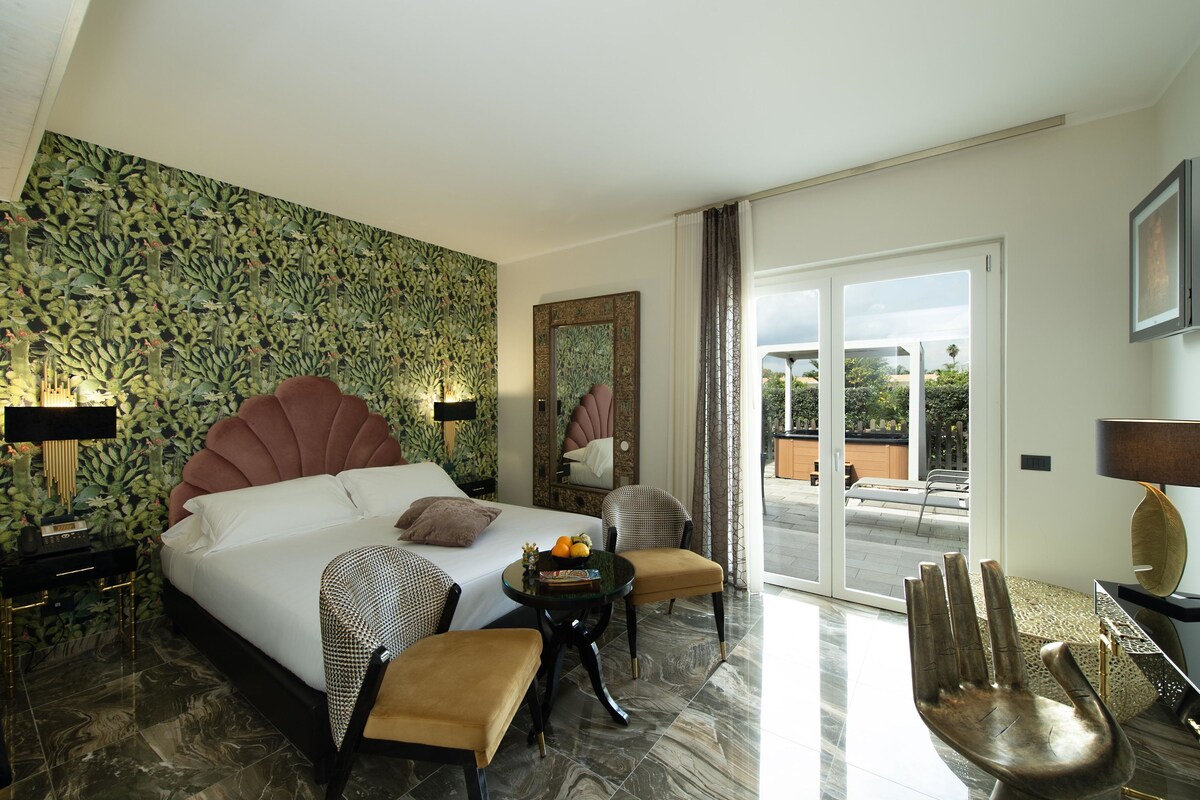 A modern hotel room with a large bed, a sitting area with a table, and a view of the outdoors.