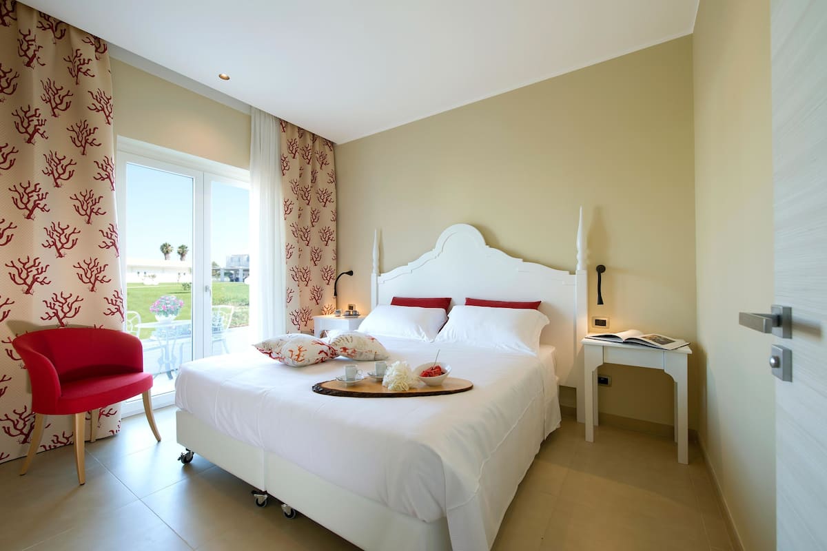 Une chambre d’hôtel avec un lit blanc, une chaise rouge et une table à manger sur laquelle se trouve un plateau de nourriture.