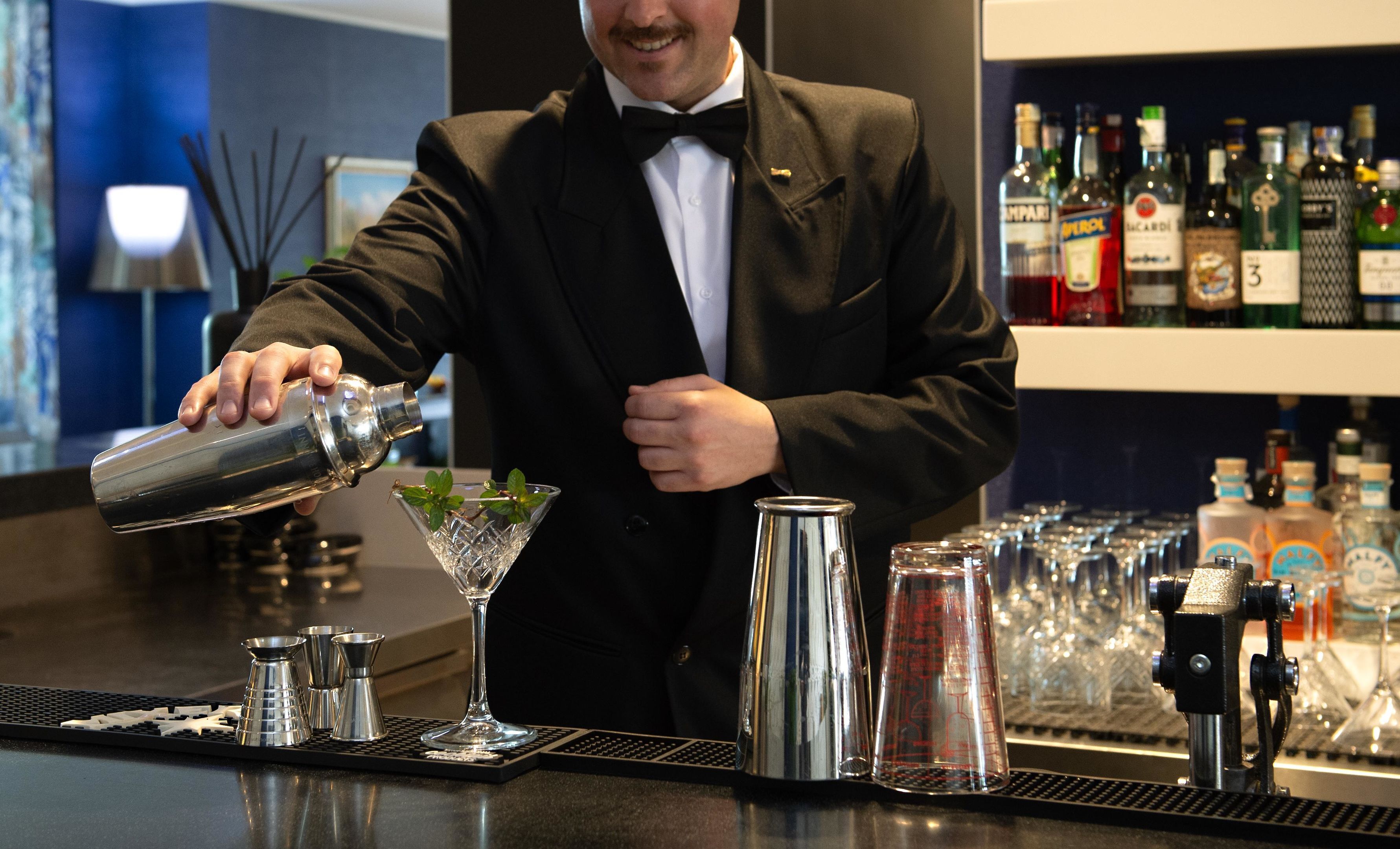 A bartender pouring a drink into a martini glass.