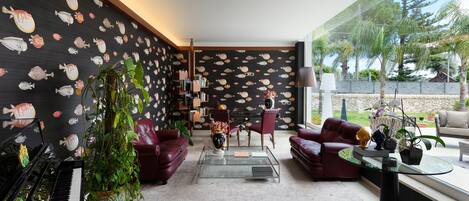Una sala de estar moderna con un piano, sofás rojos, una mesa de centro de vidrio y un ventanal con vista a palmeras.