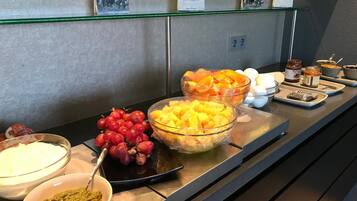 En buffet med forskellige retter, herunder druer, ananasstykker og en skål med grøn dip.