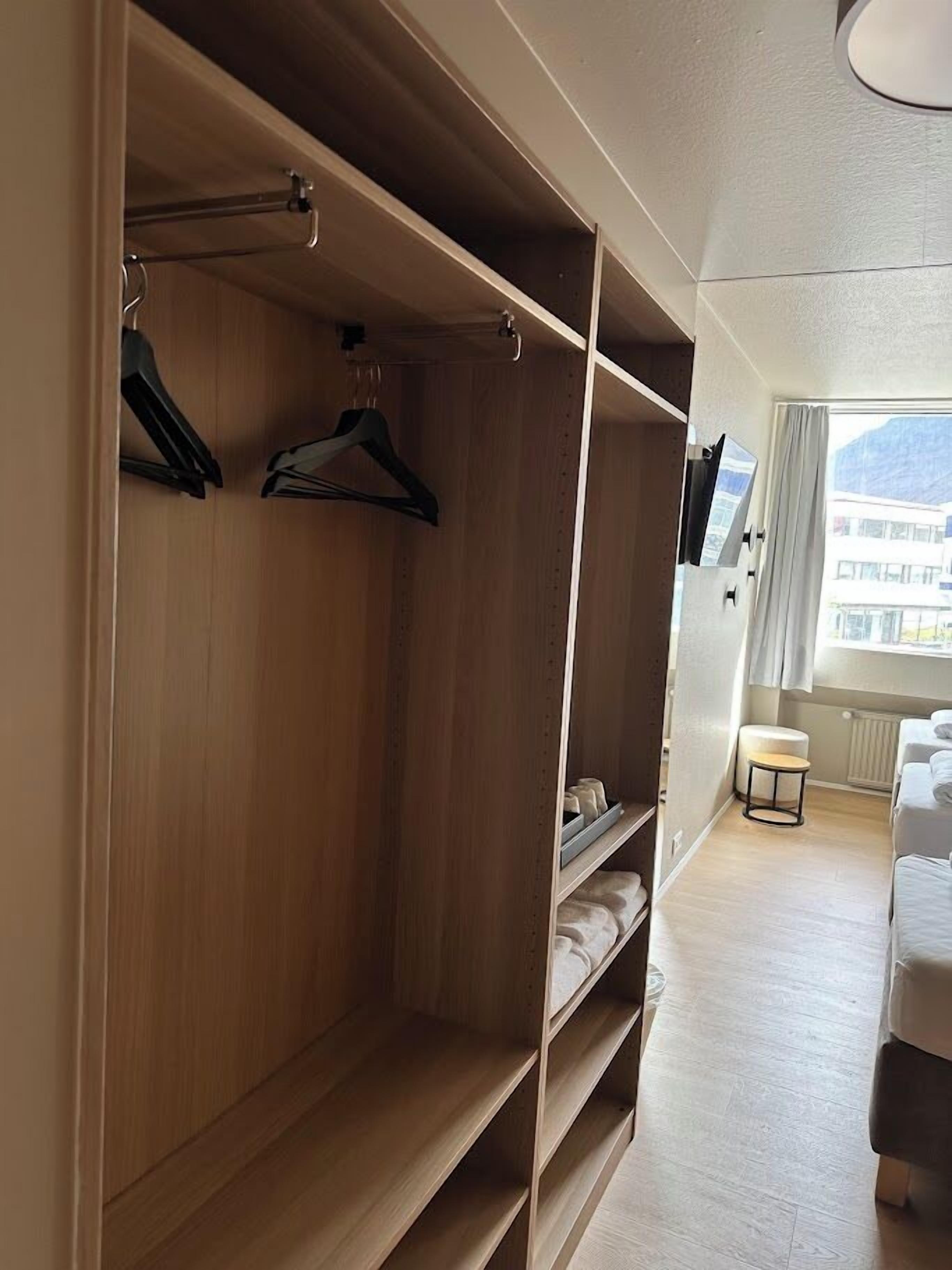 A room with a wooden wardrobe, a small table, and a bed.