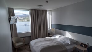 A hotel room with a bed, a chair, a nightstand, a lamp, and a view of the sea. - Hótel Ísafjörður (Isafjordur)