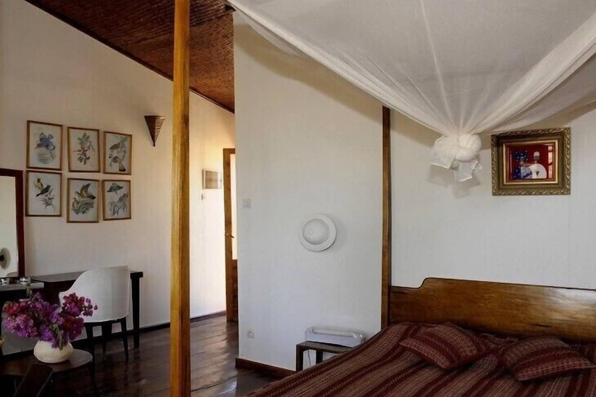 A room with a bed, a desk, and a chair. There are framed pictures on the wall.