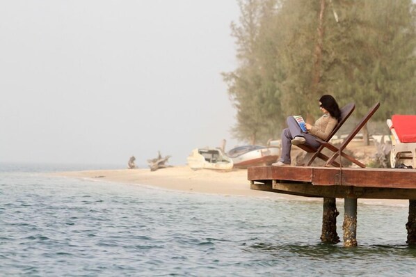 A person sitting on a wooden dock over water, reading a book. - Campement Lodge Océan & Savane (Tare)