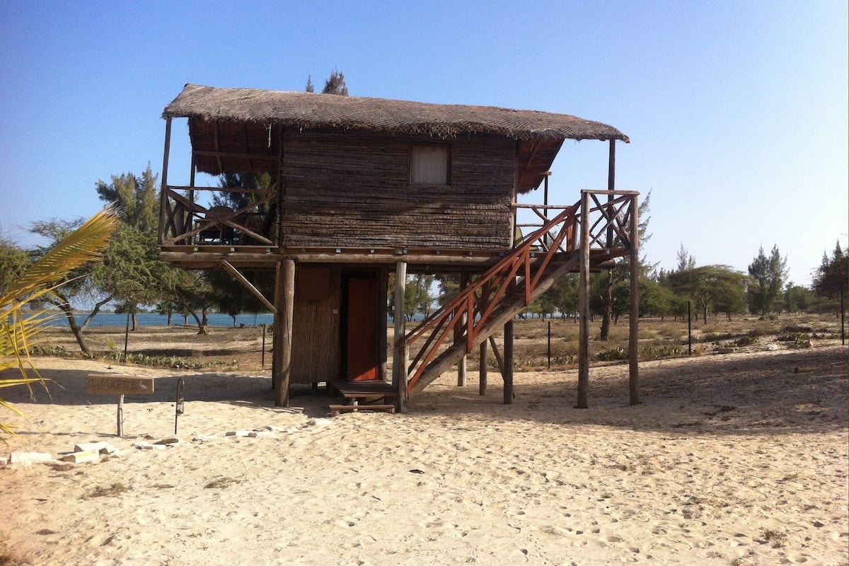 A wooden structure with a thatched roof, a staircase, and a small porch area.