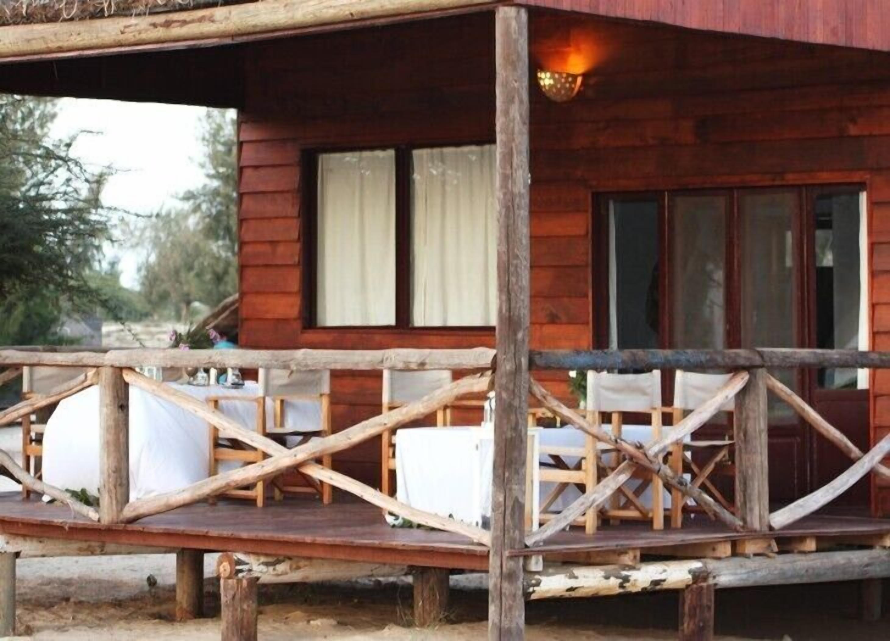 Une cabane en bois avec une véranda, des rideaux blancs et une table avec des chaises.