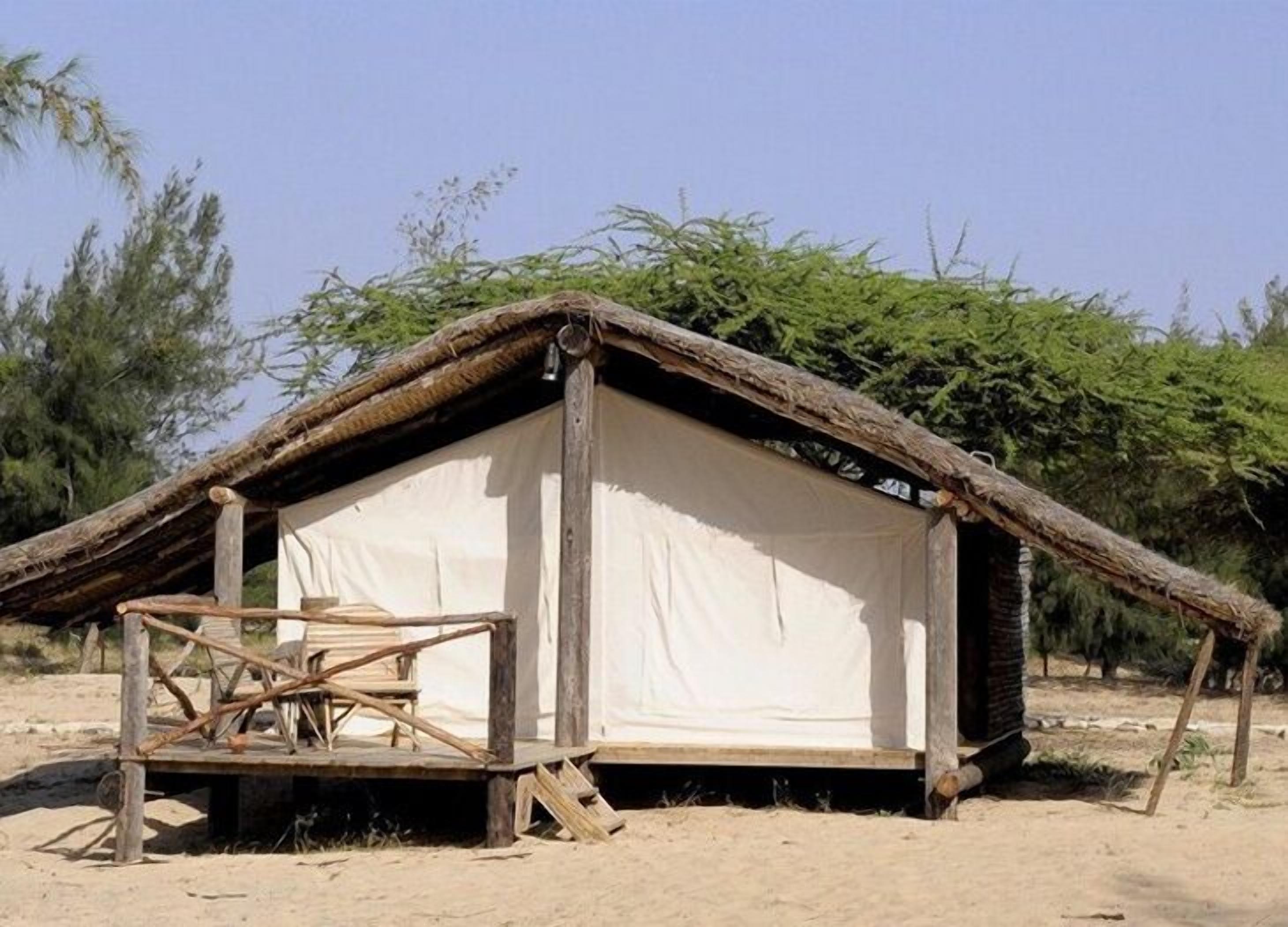 A simple, single-room structure with a thatched roof and a white canvas wall, surrounded by sparse vegetation.