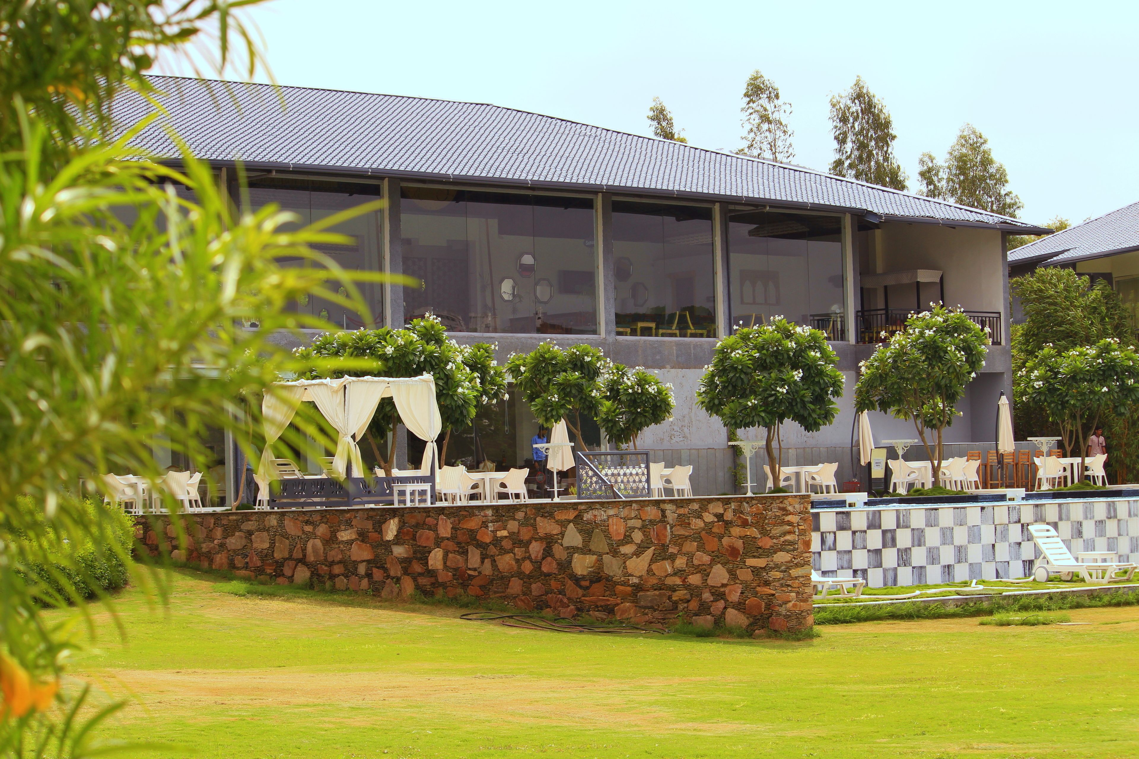 A modern building with a stone wall and a balcony with white chairs and umbrellas.