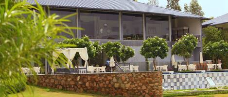 A modern building with a stone wall and a balcony with white chairs and umbrellas.