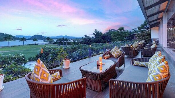An outdoor seating area with wicker furniture and cushions, overlooking a landscaped garden and a body of water with distant hills.