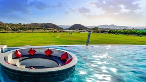 A swimming pool with a hot tub and red cushions, surrounded by a lush green landscape and mountains in the background.