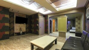 A spacious living area with a sofa, a coffee table, and a TV. There is a door leading to a bedroom and a bathroom. - Brown Hotel (Suncheon)