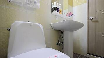 Un baño con inodoro, lavabo y ducha. Hay artículos de aseo en la repisa sobre el lavabo.