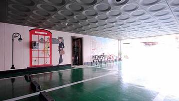 A spacious lobby with a green floor, a red telephone booth, and a mural on the wall.