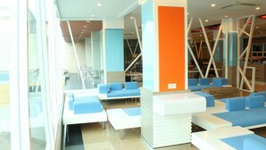 A modern indoor seating area with blue and white furniture, a central orange pillar, and a view through large windows. - Chariot Pattaya Residence (Pattaya)