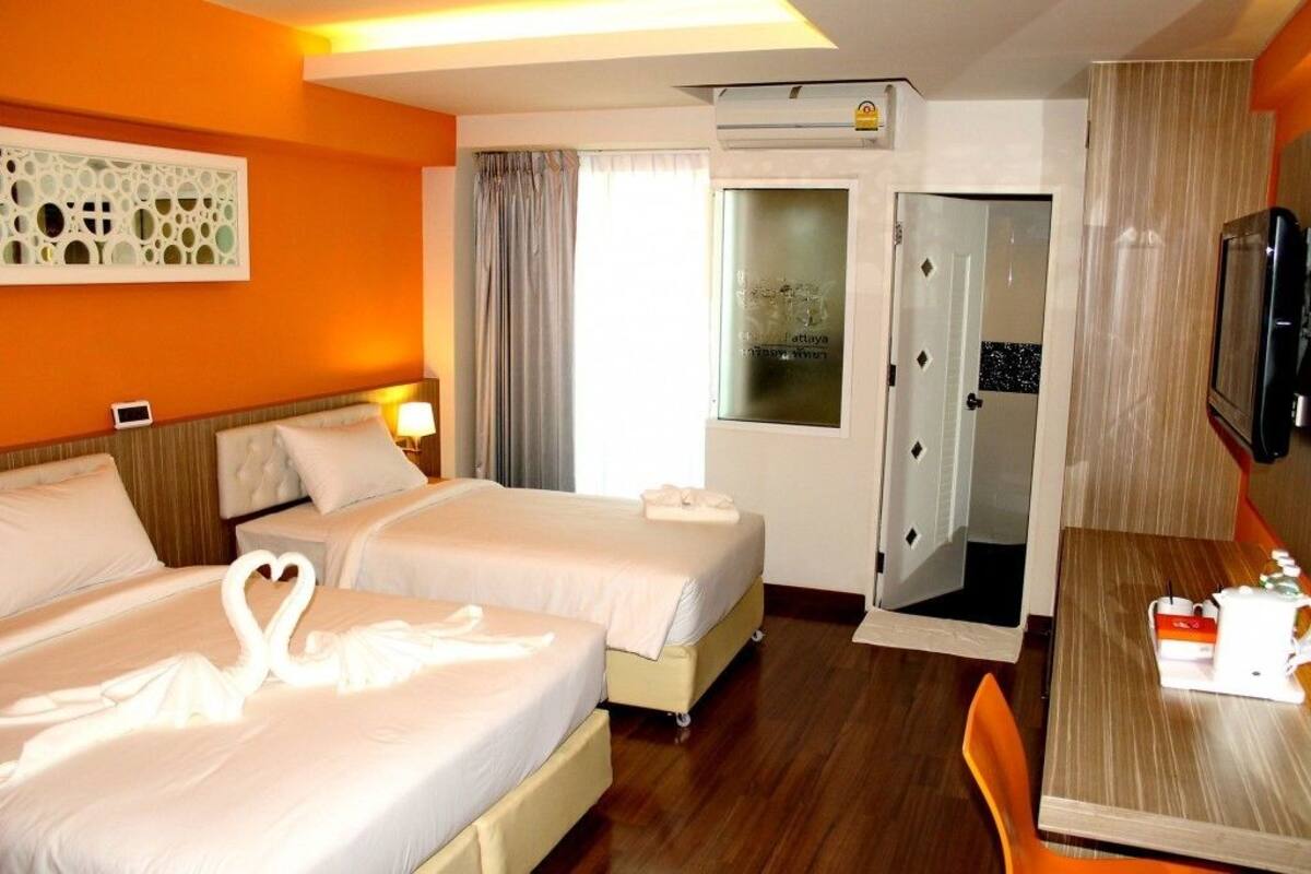 Habitació d'hotel amb dos llits, un televisor, escriptori amb cadira i finestra amb cortines.