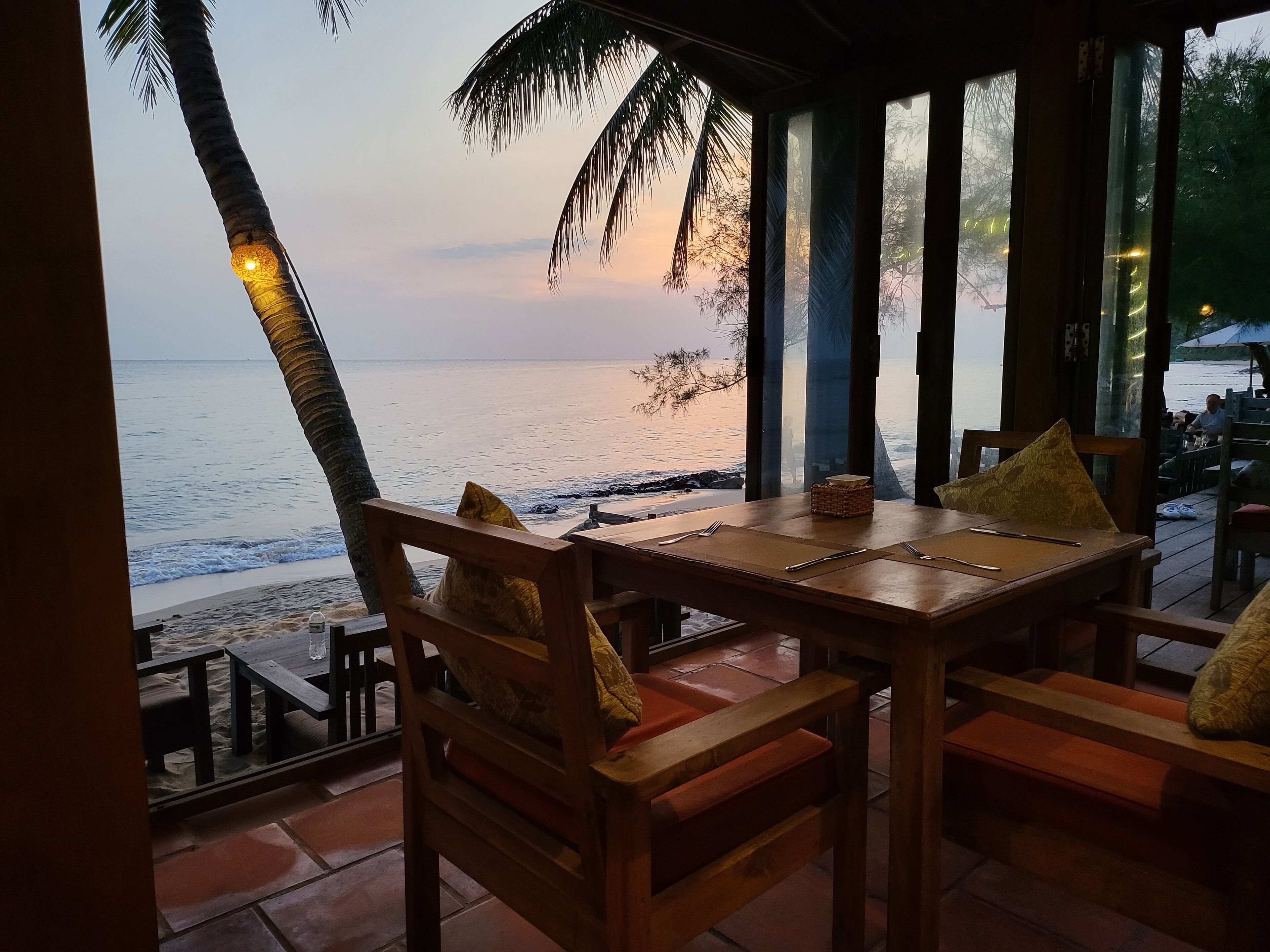A wooden table with chairs and a view of the beach and ocean.