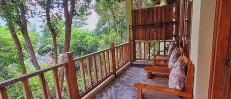 A wooden balcony with a tiled floor, wooden railings, and a seating area with cushions.
