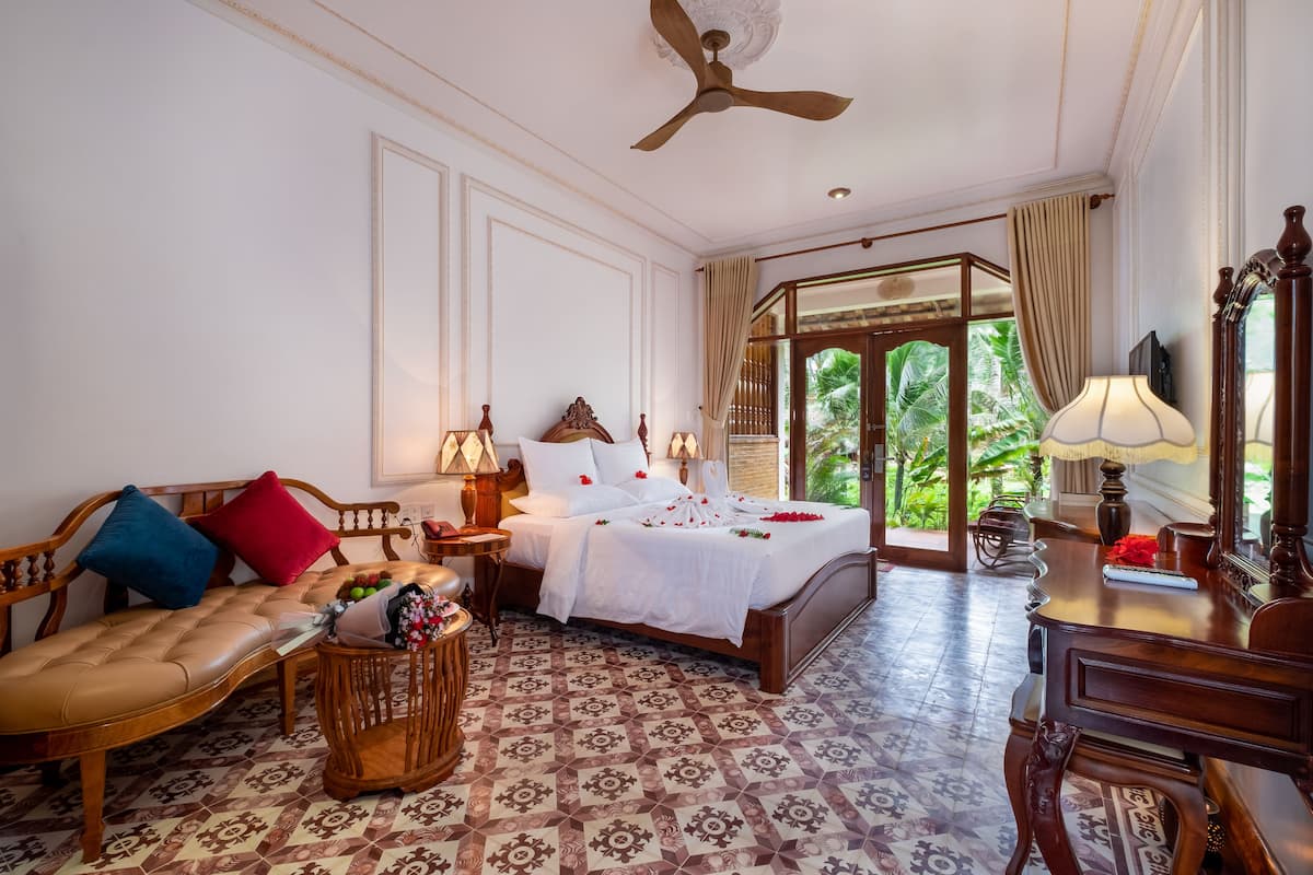 A hotel room with a bed, a sofa, a desk, and a ceiling fan.
