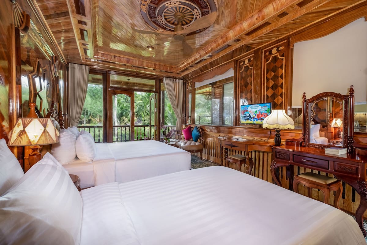 A room with two beds, wooden ceiling, large windows, a desk, and a mirror.